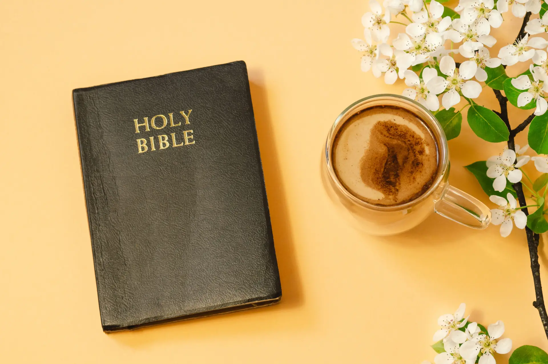 A bible sitting next to a coffee cup and cut flowers with an orange background