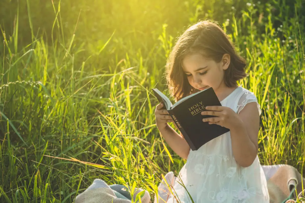 young girl sitting in a field reading her bible showing why biblical integration is important