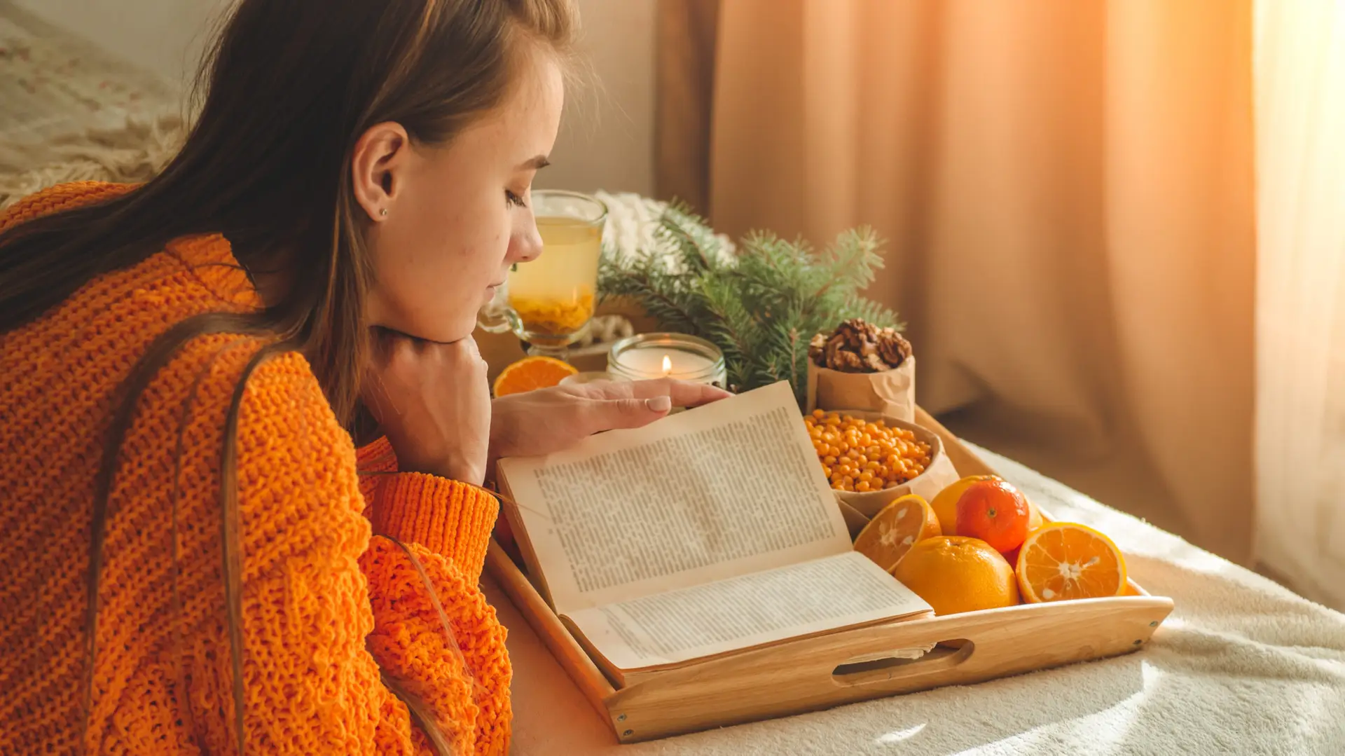 Woman wearing an orange sweater reading a book on biblical worldviews with snacks around her