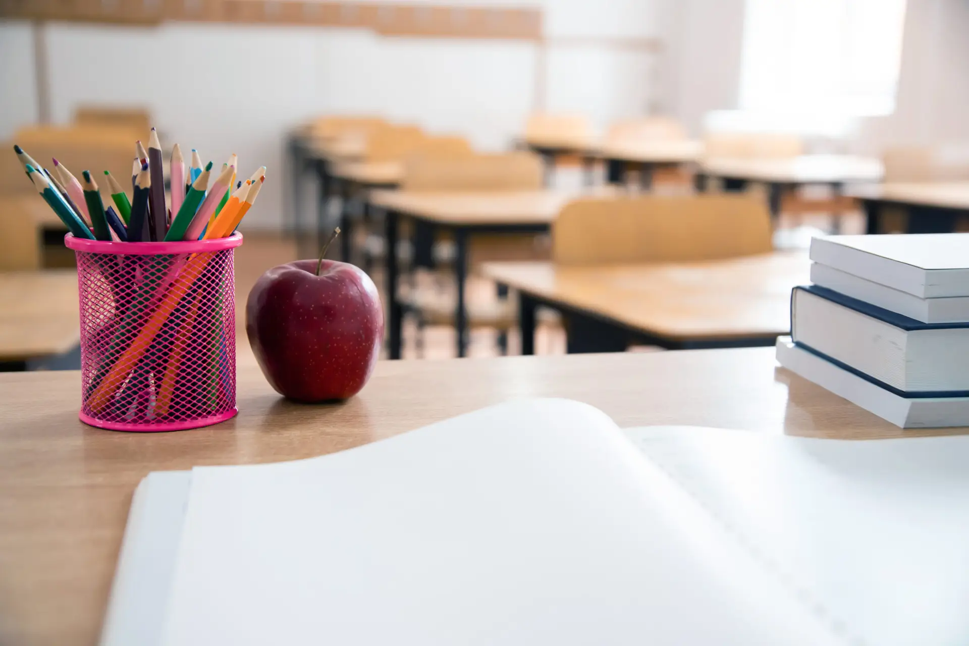 an open notebook on a teacher's desk with pencils and an apple overlooking the classroom in a christian education school